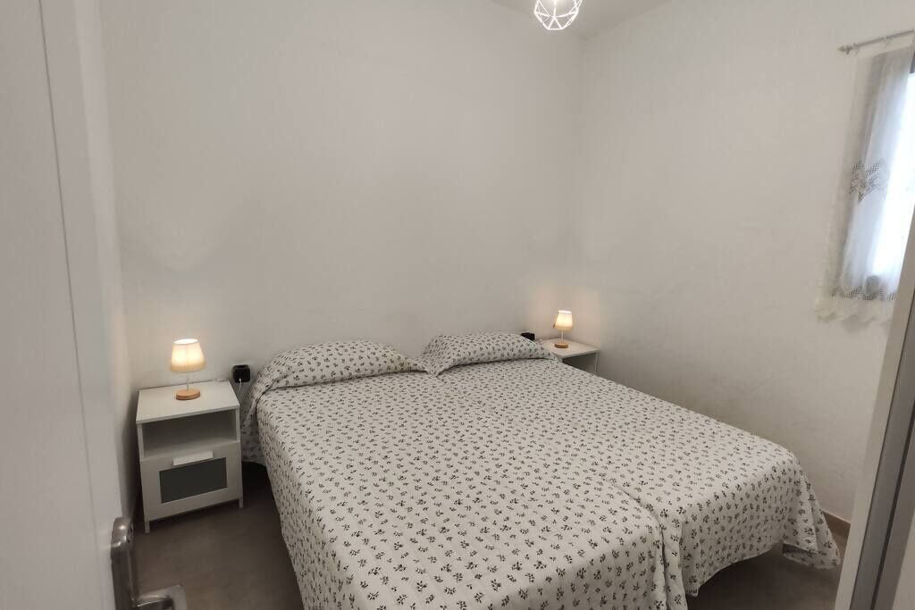 A small, simple bedroom with a bed, two bedside tables, and a window.
