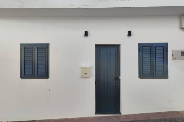Un edificio blanco con una puerta central y dos ventanas con contraventanas.
