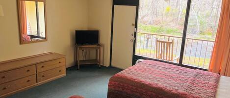 Une chambre d’hôtel avec deux lits, une commode, un téléviseur posé sur une petite table et un balcon donnant sur la verdure.