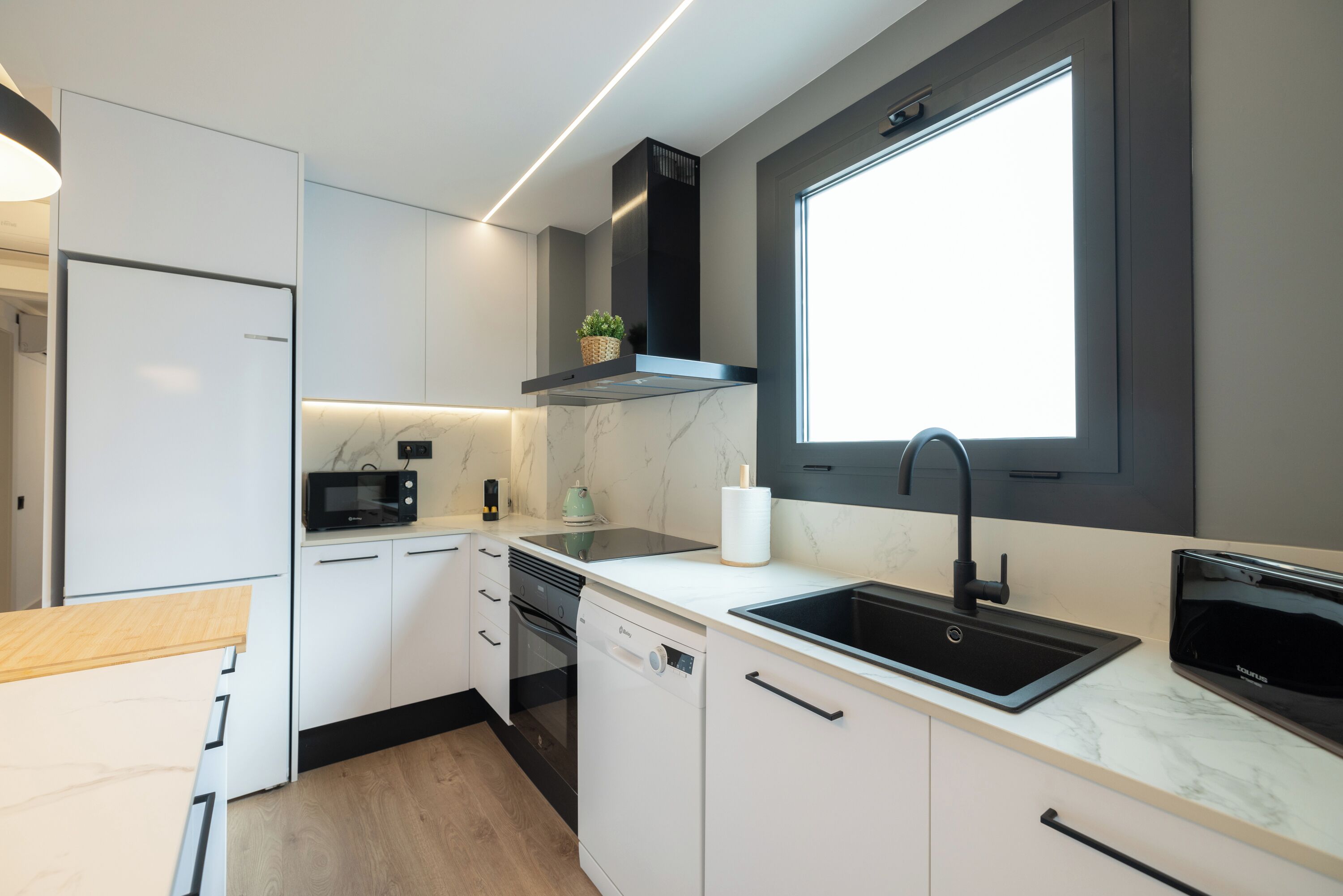 Une cuisine moderne avec des meubles blancs, une cuisinière noire, un four à micro-ondes et un évier.