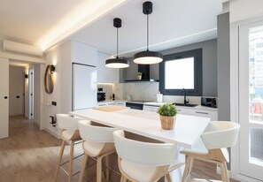 A modern kitchen with a central island, white bar stools, pendant lighting, and a large window. - Stay U-nique Apartment Villarroel (Barcelona)