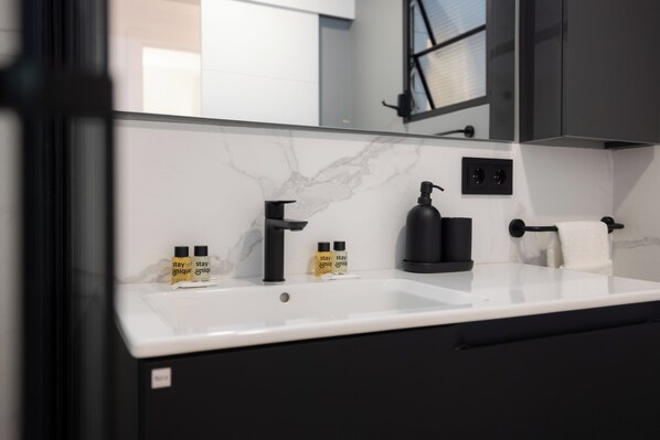 A modern bathroom with a white marble countertop, black fixtures, and two bottles of 'stay unique' hand soap. - Stay U-nique Apartment Villarroel (Barcelona)