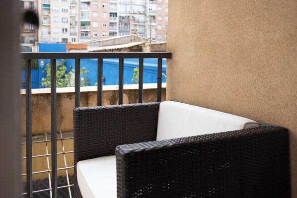 Un balcón con mobiliario de mimbre y vista a un edificio azul al fondo.