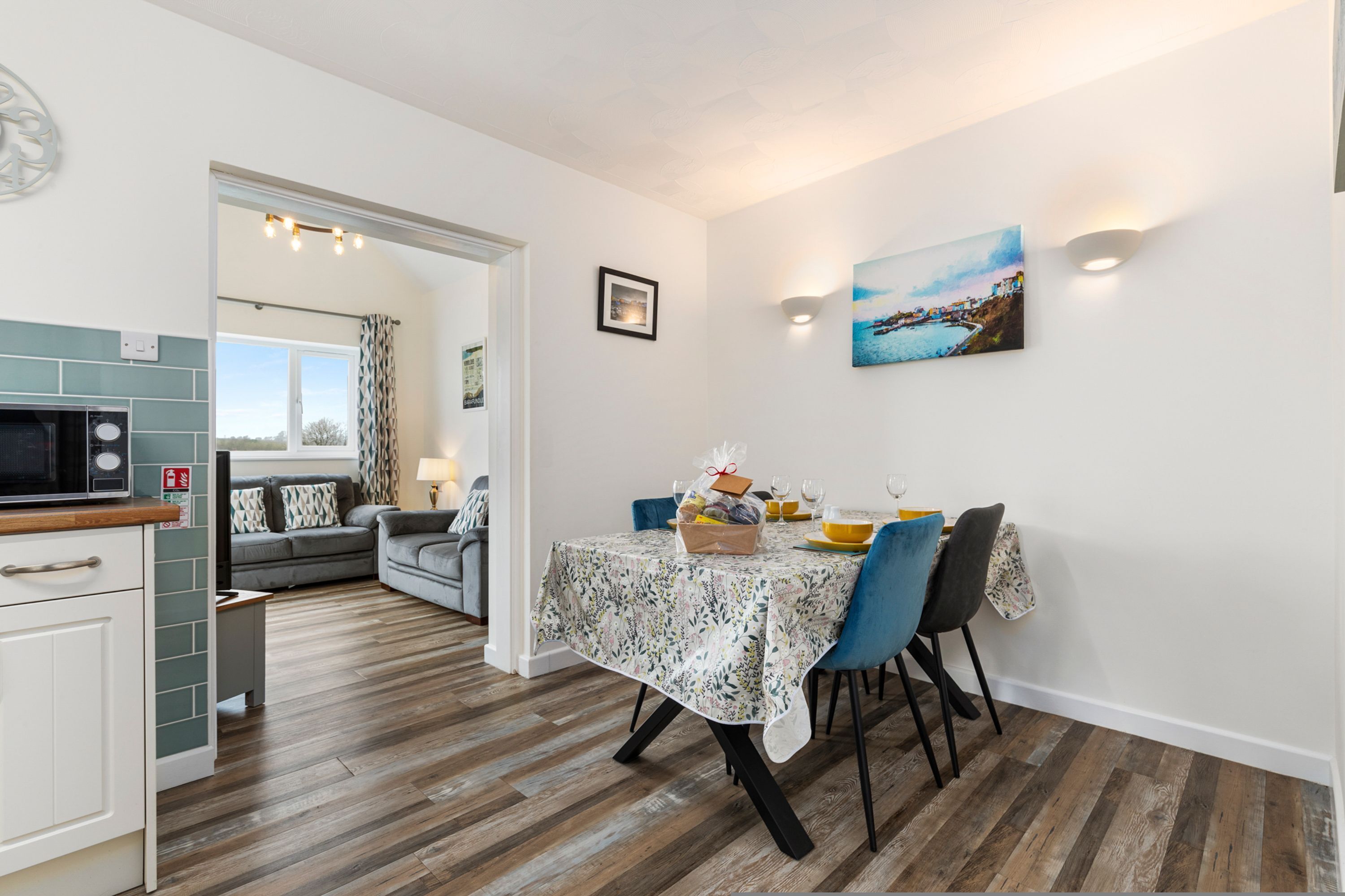 Un coin repas avec une table dressée pour quatre personnes, une cuisine équipée d’un four à micro-ondes et une vue sur l’extérieur par une porte.