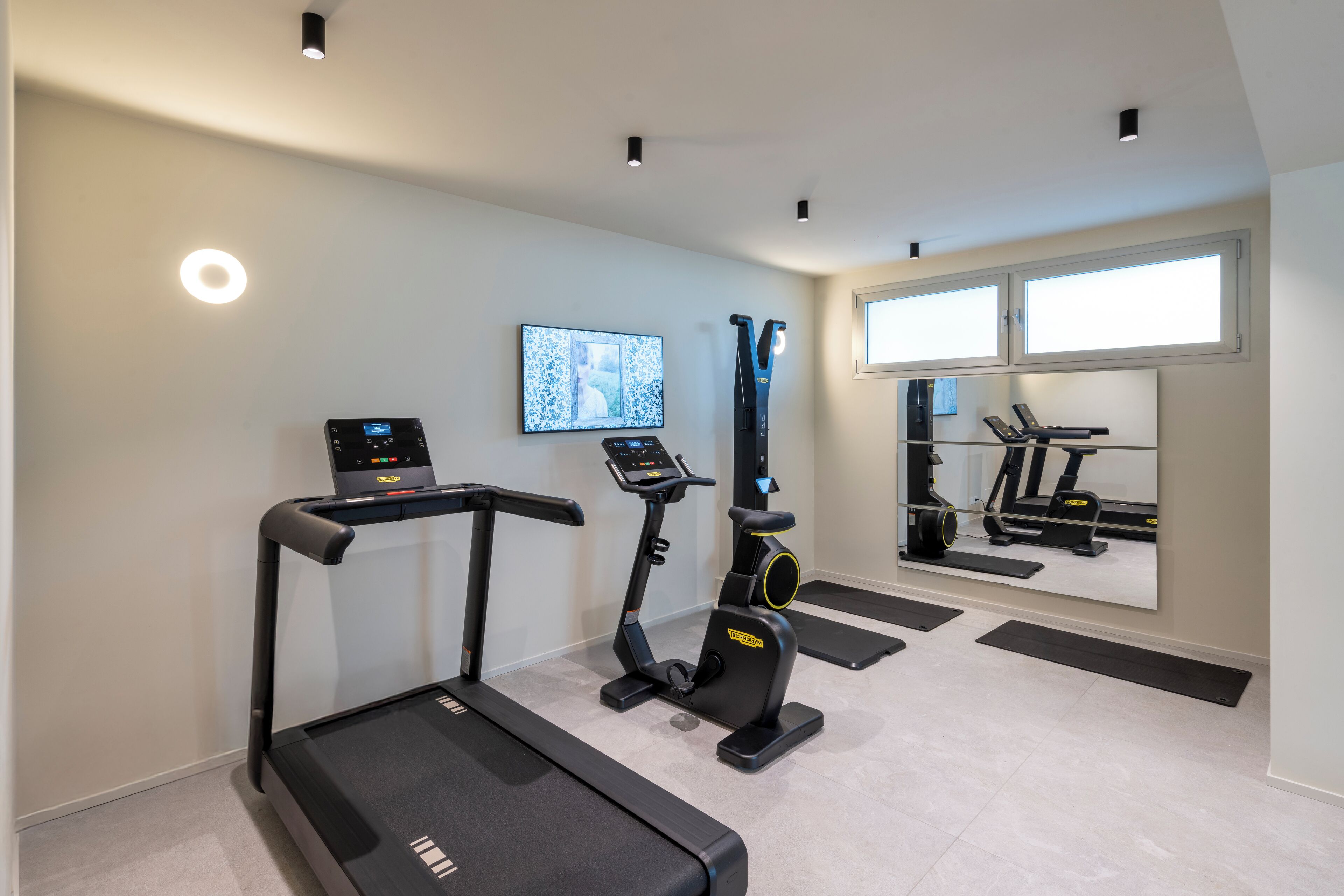 A home gym with a treadmill, elliptical, and stationary bike, a TV, and a large mirror reflecting exercise equipment.
