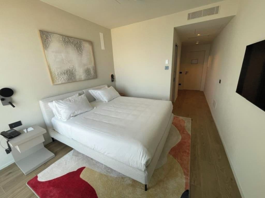 A modern bedroom with a large bed, bedside tables, a flat-screen TV, and a painting on the wall.
