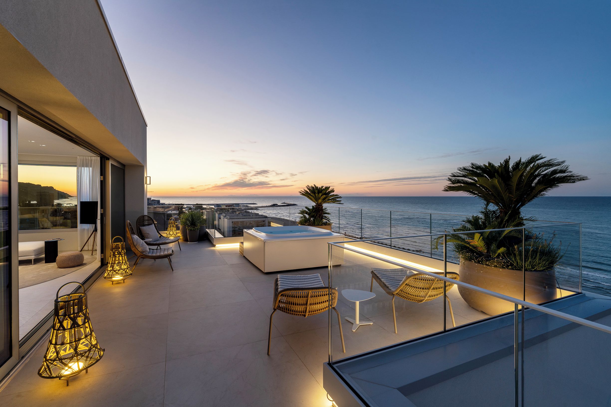Una terraza moderna al aire libre con asientos, piscina y vista al mar al anochecer.