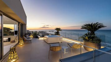 Una terraza moderna al aire libre con asientos, piscina y vista al mar al anochecer.