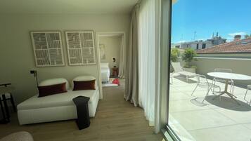 Una habitación de hotel moderna con un ventanal grande, un sofá con cojines, una mesita y un adorno de pared decorativo.