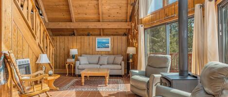 Un interior de madera acogedor con un sofá, sillas, un sillón mecedora y una chimenea.