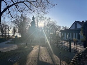 Ein gepflasterter Weg führt zu einem befriedeten Bereich, rechts befindet sich ein Gebäude.