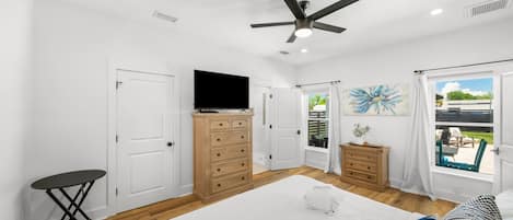 Un dormitorio con cama, cómoda, televisor, ventilador de techo y ventana con vistas al exterior.