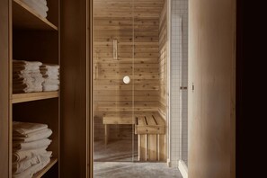 A wooden interior with a bench, shelves with folded towels, and a tiled wall. - The Pioneer | BESIDE's very first cabin (Lanaudière)