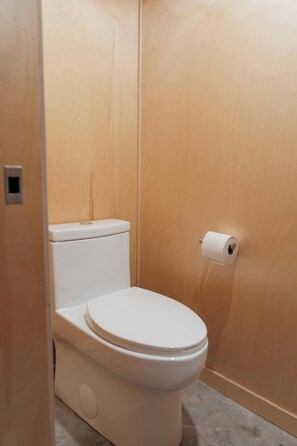 A small, enclosed bathroom with a toilet, a roll of toilet paper, and a flush handle. - The Pioneer | BESIDE's very first cabin (Lanaudière)