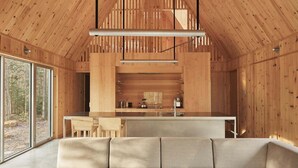 A modern interior with a wooden ceiling, a kitchen area, and a seating area with a sofa. - The Cape (Lanaudière)
