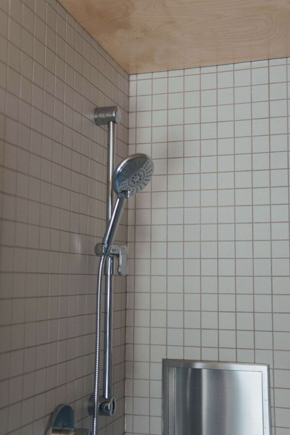 A shower with a handheld showerhead, a wall-mounted control panel, and a metal cabinet. - The Shoal (Lanaudière)