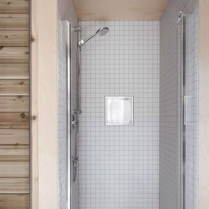 Een douche met een handdouche, een douchekop met glazen ombouw, en een vierkante spiegel aan de muur.