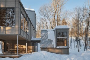 Een modern gebouw met twee verdiepingen, grote ramen, een overdekte veranda en een sneeuwbedekt dak.