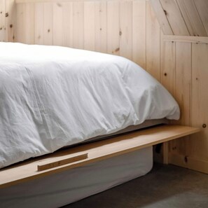 A bed with a white mattress and a wooden headboard in a room with wooden walls. - The Shoal (Lanaudière)