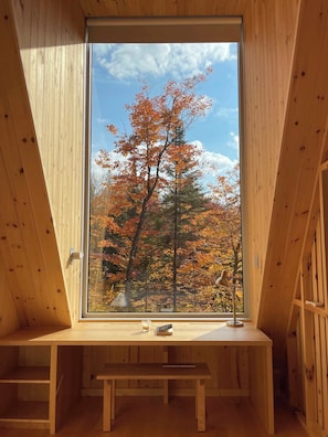 A wooden interior with a large window, a bench, and a small table with a book and a glass.