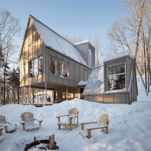 A modern house with a large window, a covered porch, and snow-covered ground.