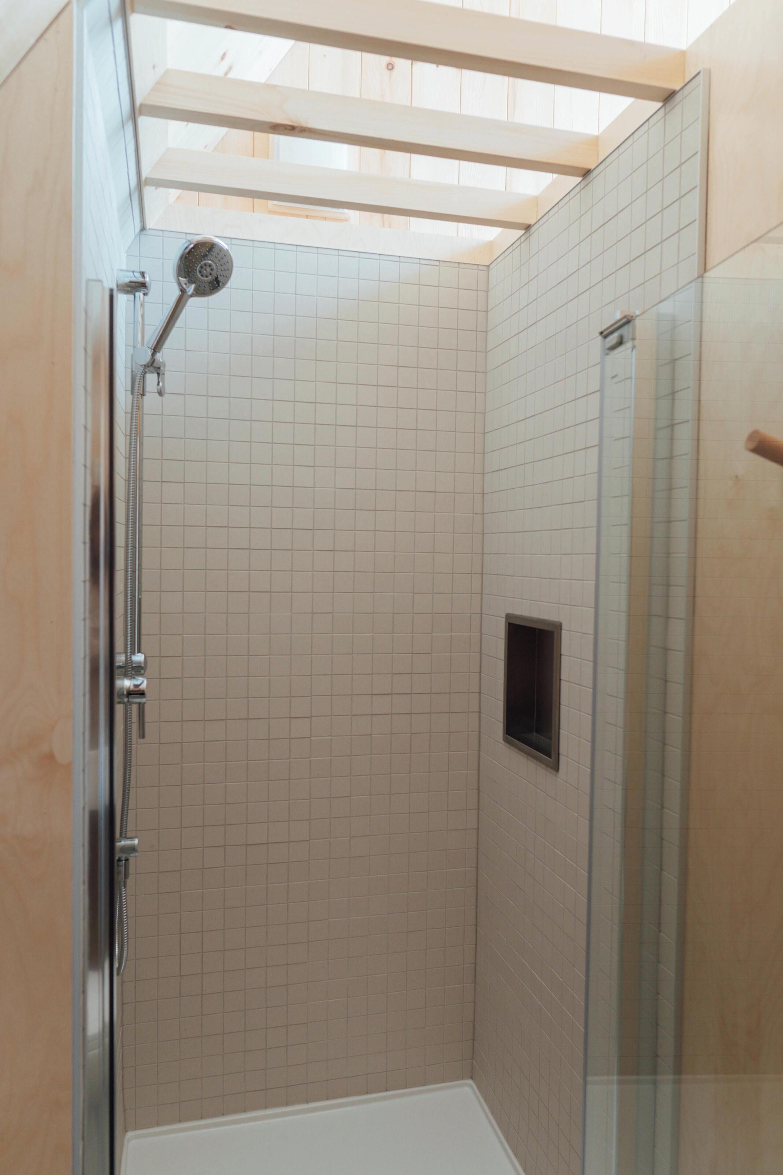 A shower with a glass door, a tiled wall, and a small window.