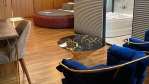 A modern room with a wooden floor, a round red sofa, a blue armchair, a small round table with a black marble top, and a large mirror. - Nuans Pansiyon (Istanbul)