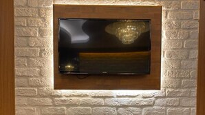 A modern living room with a TV mounted on a brick wall, a fireplace below, and a remote control on the mantel. - Nuans Pansiyon (Istanbul)