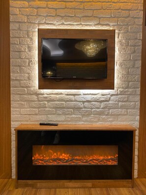 Un soggiorno moderno con una TV fissata a una parete in mattoni, un caminetto sottostante e un telecomando sul ripiano.