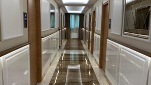 A hotel hallway with a modern design, featuring a central light fixture, marble flooring, and doors with window treatments. - Nuans Pansiyon (Istanbul)