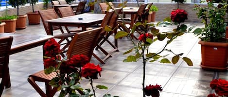 An outdoor patio with wooden tables and chairs, potted plants, and red roses.