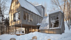 Ein modernes Haus mit einem großen Fenster, einer Veranda und schneebedecktem Grund.