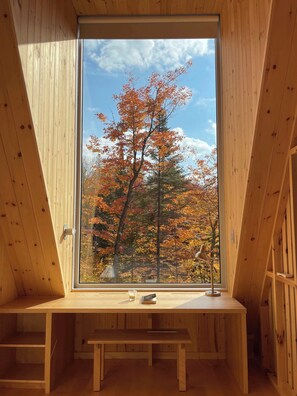 A wooden interior with a large window, a bench, and a small table with a book and a glass. - The Shoal (Lanaudière)