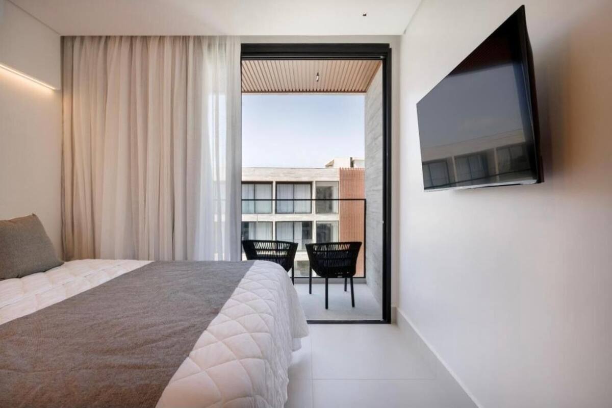 Ein modernes Hotelzimmer mit Bett, Flachbildfernseher, Balkon mit Sitzgelegenheiten und Blick auf Gebäude.