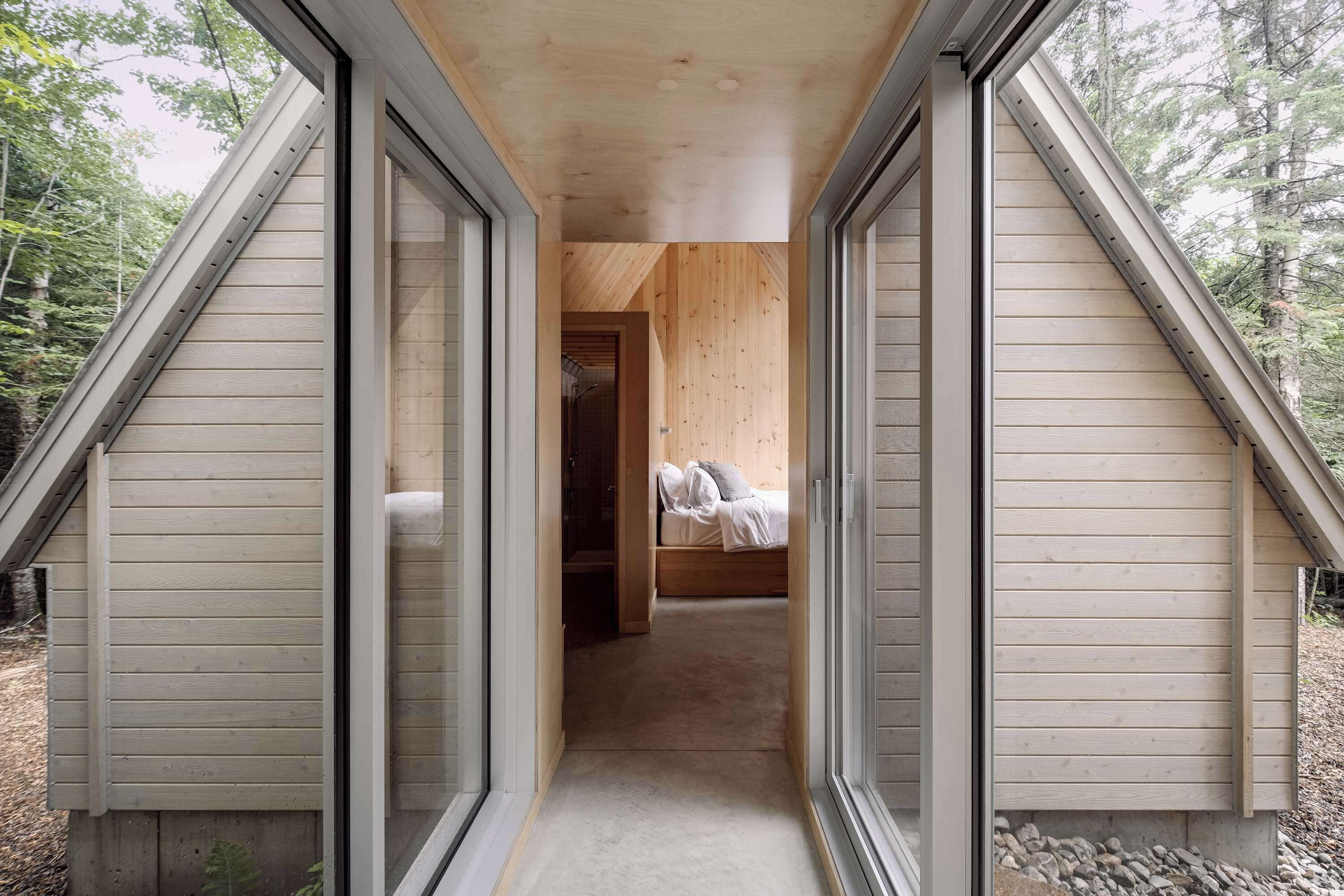 A bedroom with a bed, a wooden ceiling, and a view of the forest.
