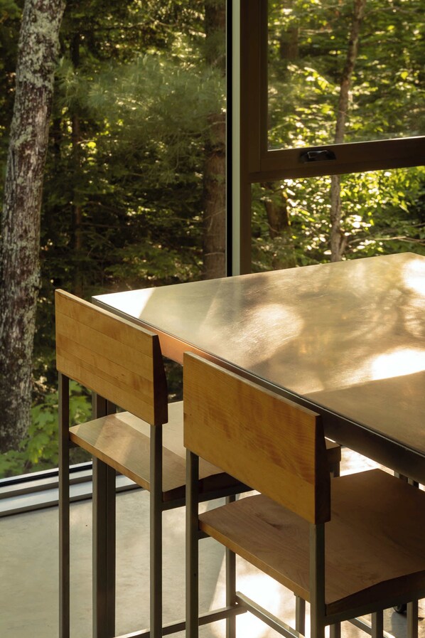A table with wooden chairs, a metal frame, and a view of trees through a window.