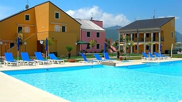 A swimming pool with blue lounge chairs, a yellow building, and a pink building in the background.