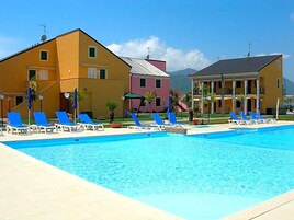 Una piscina con sillas reclinables azules, un edificio amarillo y un edificio rosa al fondo.