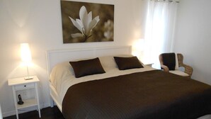 A bedroom with a bed, white nightstand, and a chair.