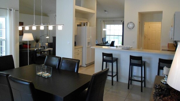 A modern kitchen with white cabinets, a dining area with a black table and chairs, and a small island with stools.
