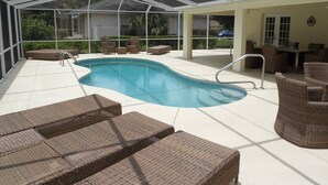 A covered outdoor swimming pool with lounge chairs, a pool ladder, and a view of the surrounding greenery.