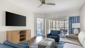 A modern living room with a flat-screen TV, a ceiling fan, and a large window offering a view of the outdoors. - Charming 1-bedroom apartment with fitness room, WiFi in Celebration (Celebration)