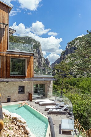 A modern building with a swimming pool, lounge chairs, and a view of mountains. - LA FORESTALE Luxury Ecolodge (Acqualagna)
