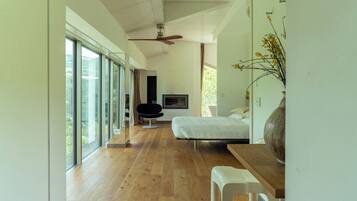 Un dormitorio moderno con un ventanal grande, una cama, un televisor y suelo de madera.