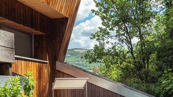 A wooden deck with white lounge chairs and planters, overlooking a lush landscape.
