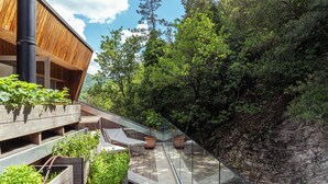 A modern building with a sloped roof, wooden exterior, and a glass balcony overlooking a lush garden and rocky hillside. - LA FORESTALE Luxury Ecolodge (Acqualagna)
