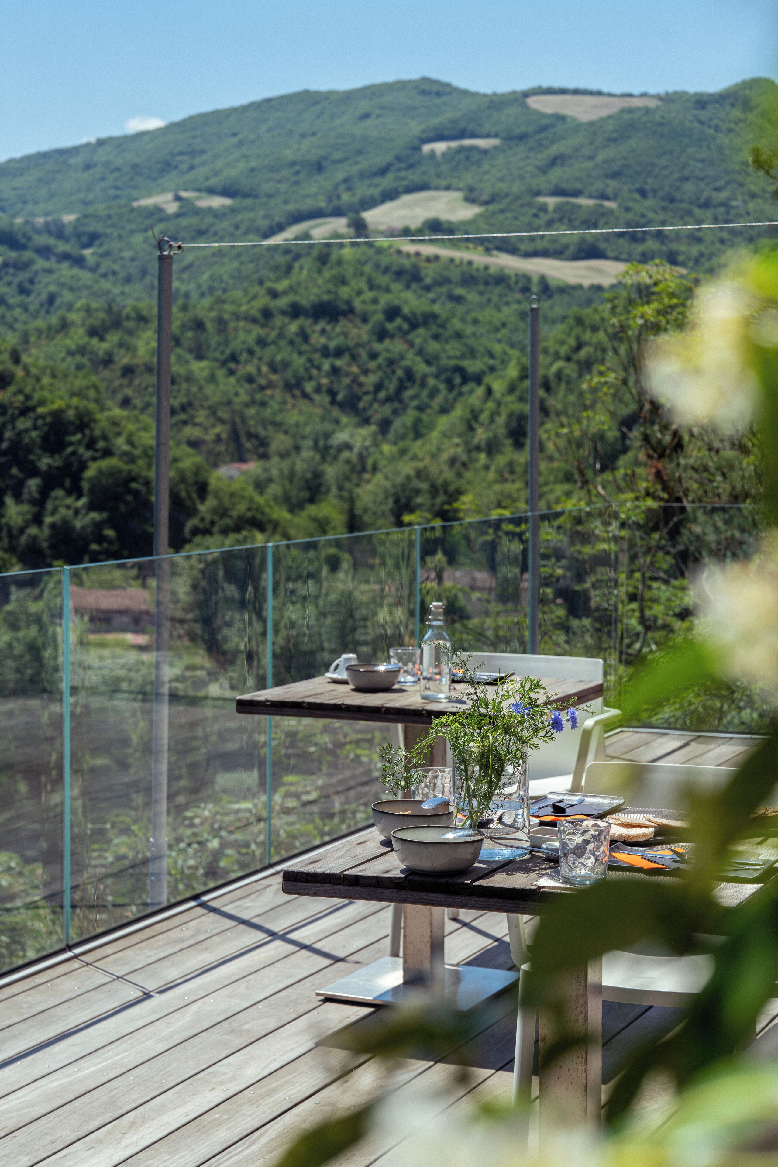 A wooden deck with a table set for dining, overlooking a lush green landscape with hills.