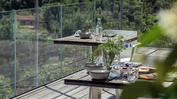 A wooden deck with a table set for dining, overlooking a lush green landscape with hills.