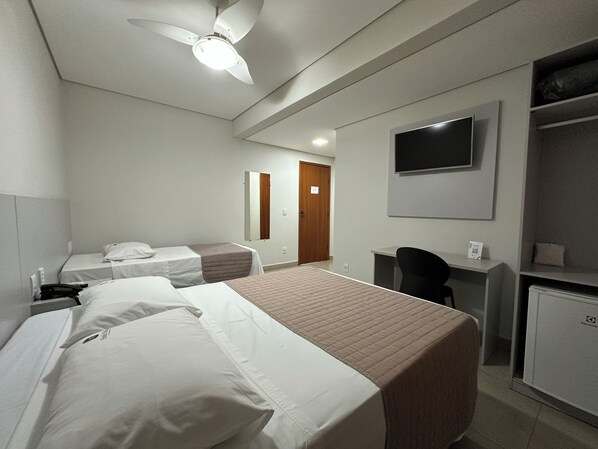 Une chambre d’hôtel avec deux lits simples, un bureau, une chaise, une télévision et une armoire.