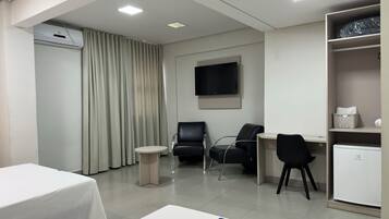 A hotel room with two beds, a desk, two chairs, a TV, an air conditioning unit, and a wardrobe.